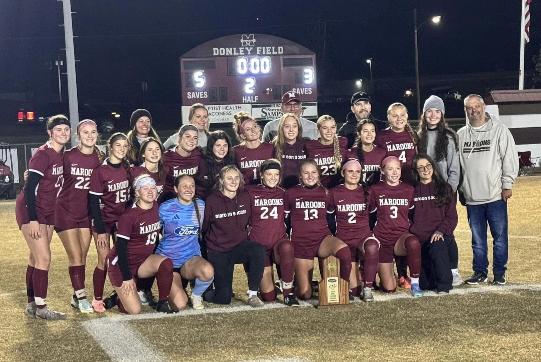 Soccer team wearing maroon uniforms with trophy in front of them