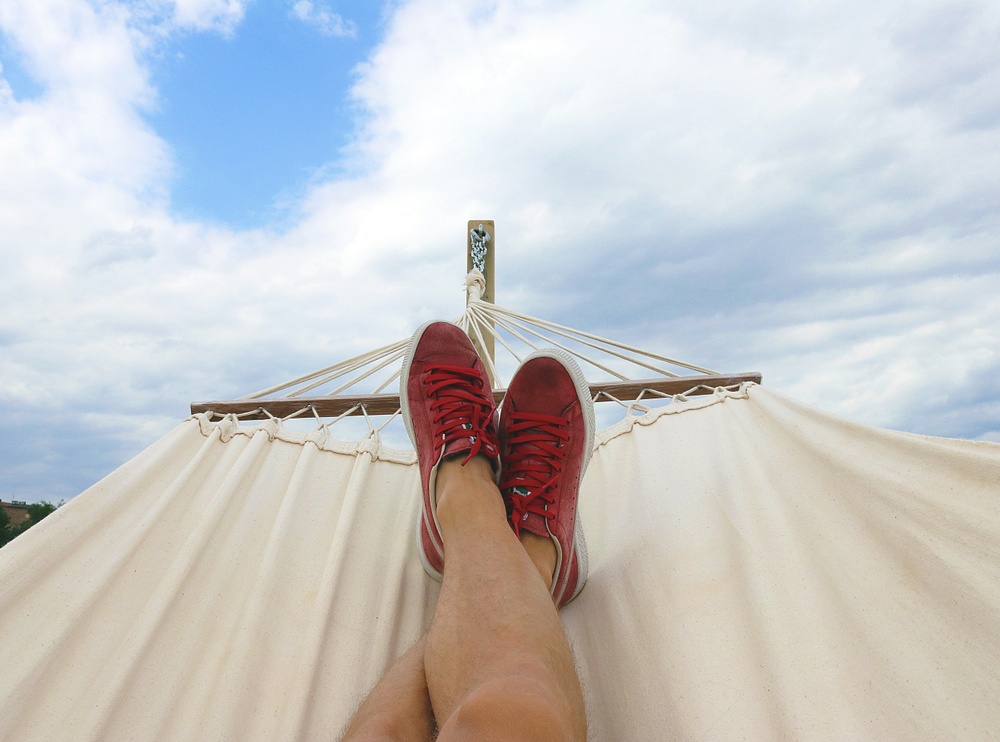 Two feet sticking out of a hammock, dressed in red shoes against a blue sky.