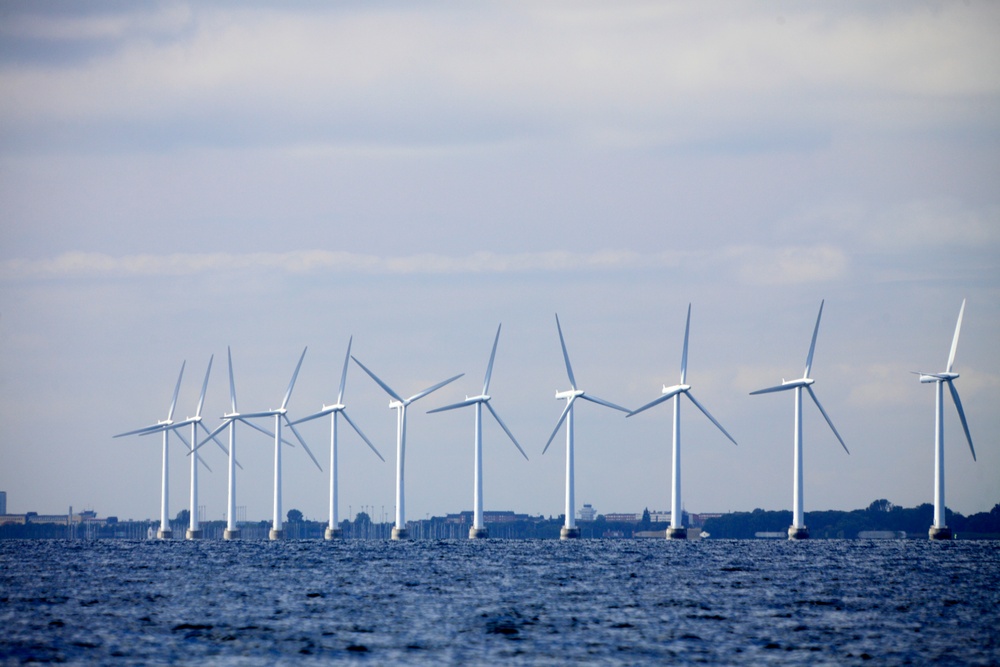 Flera vindkraftverk står på rad i havet med mulen himmel i bakgrunden.