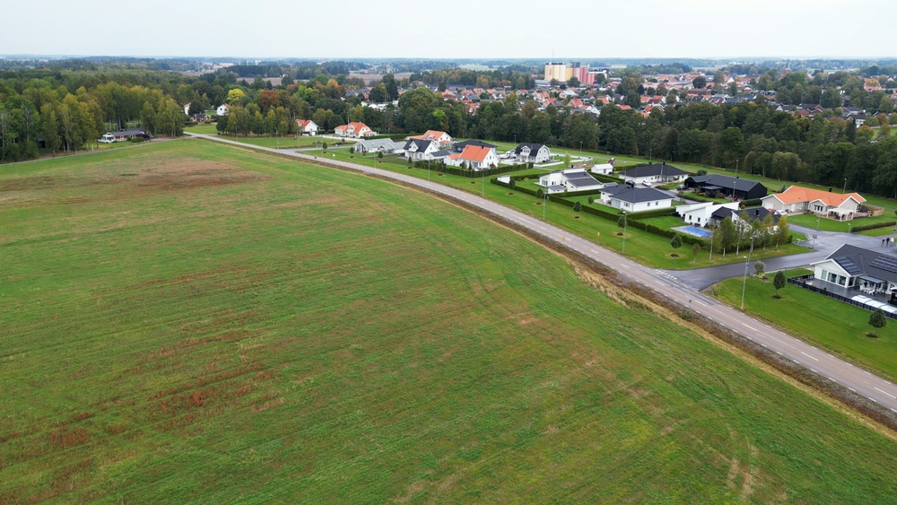 Drönarbild över en markyta där första etappen på Brännebacka västra kommer att byggas. På bilden syns även Trökörnavägen och bebyggelsen på andra sidan vägen, Brännebacka östra. Överst i bild ser man Grästorps tätort. 