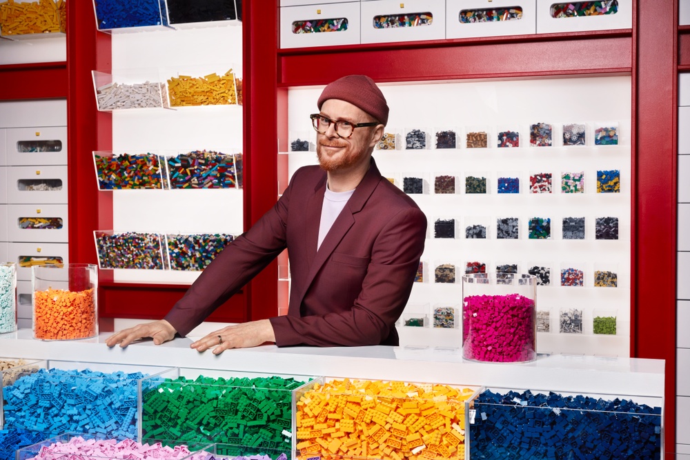 Magnus Göransson i en snygg röd mössa står och ser finurlig ut i ett rum fullt av Lego.