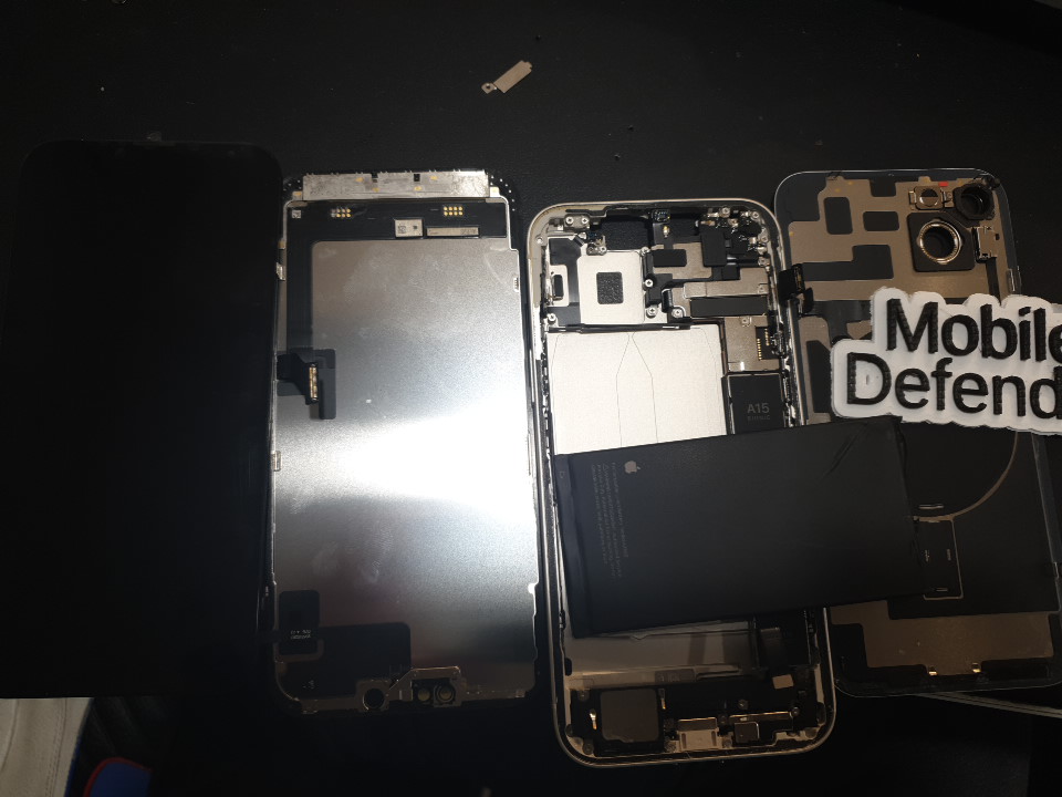 Dismantled iPhone 14 Plus on a workbench, possibly during drying and cleaning to repair water damage. Components and screen set apart for inspection.<br>