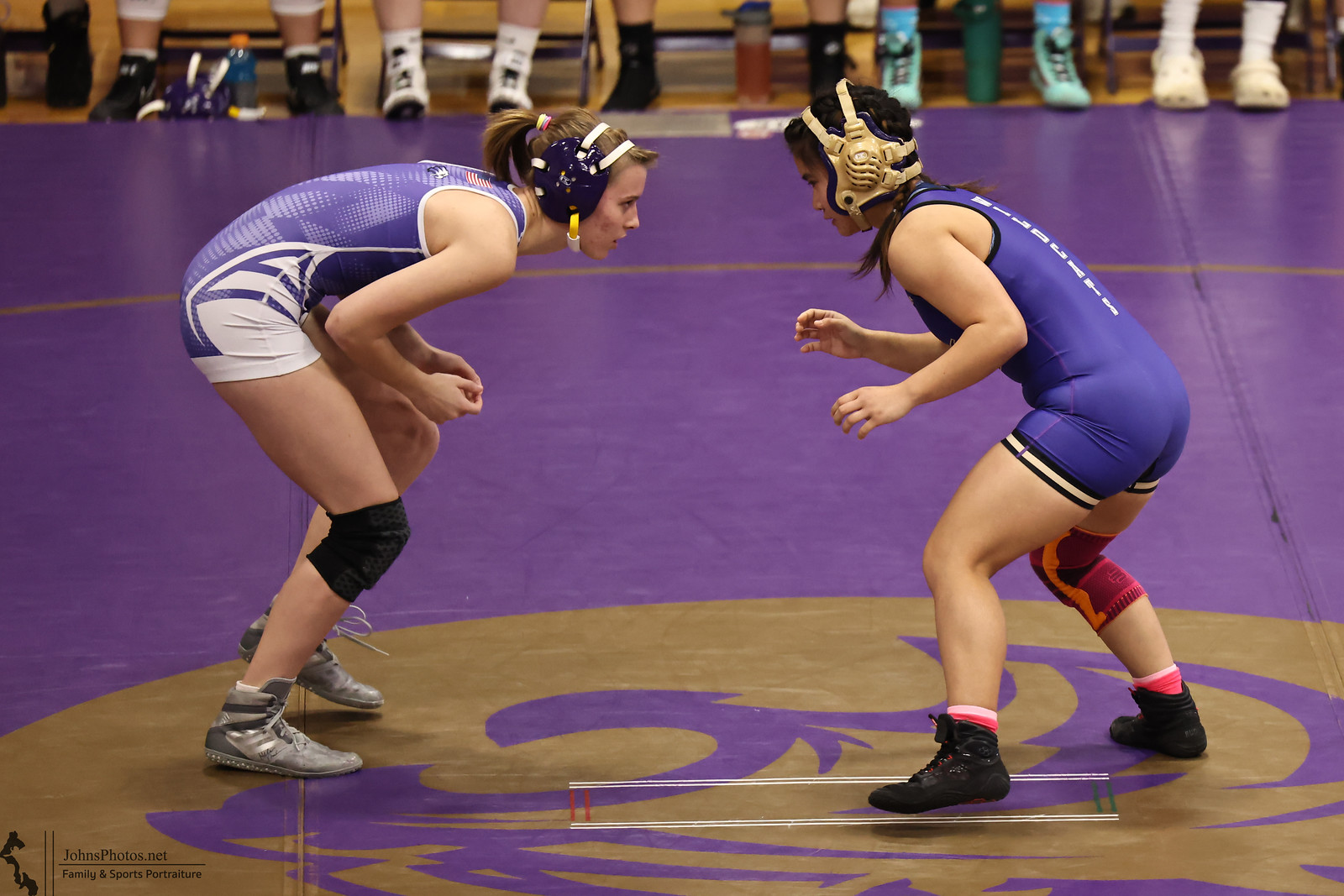 Two female wrestlers face each other in a competitive match, ready to grapple.