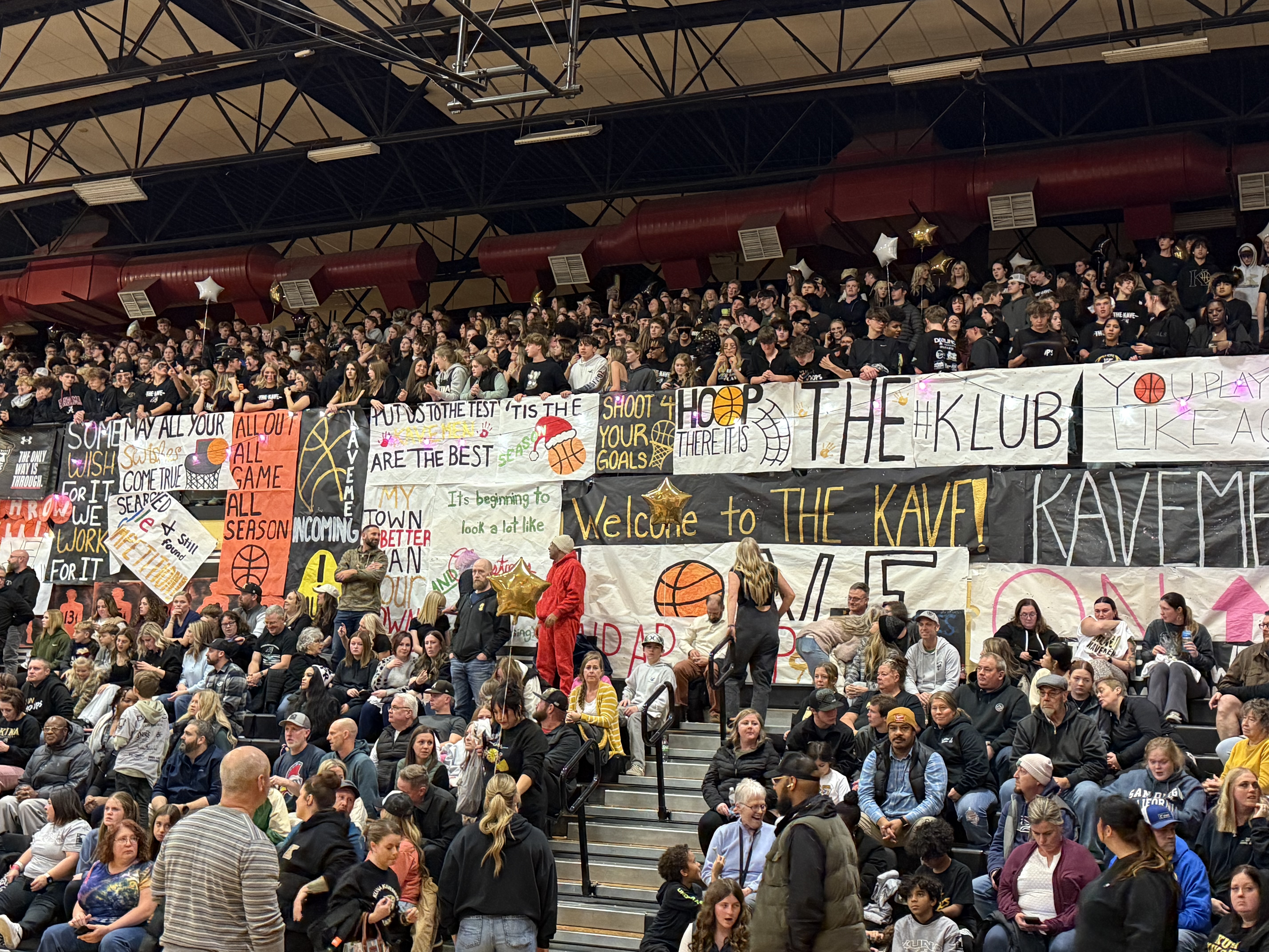 A crowd of people cheer at a basketball game, holding signs.