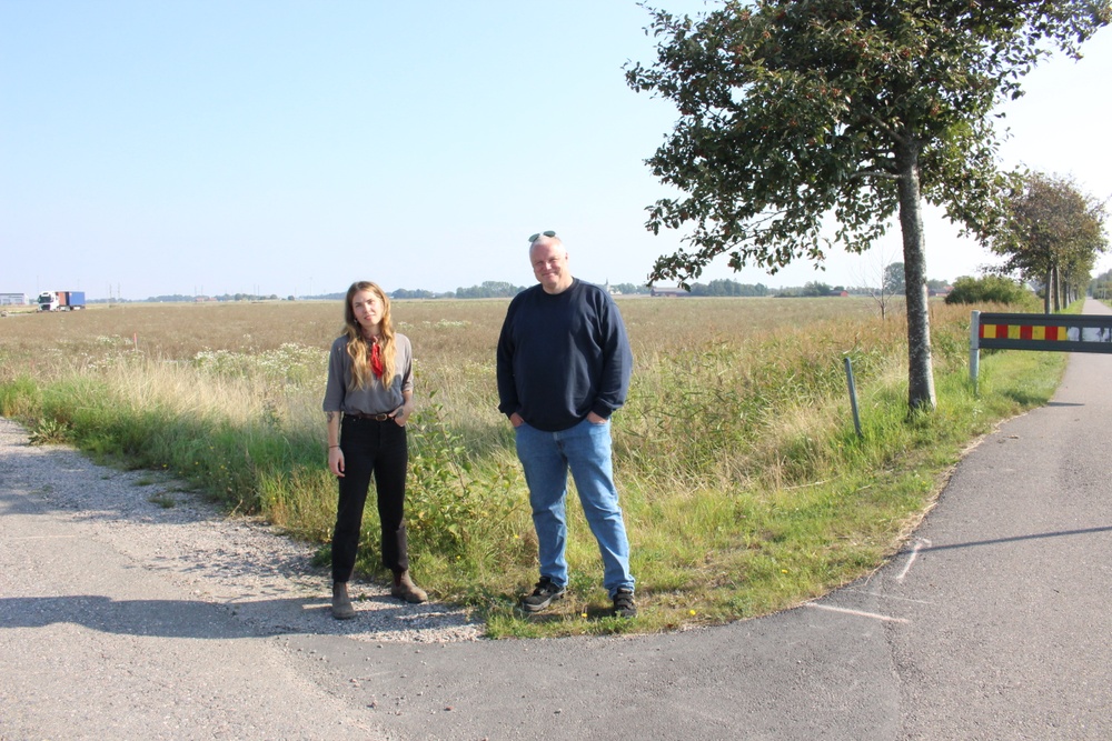En kvinna och en man står i ett vägskäl framför ett fält.