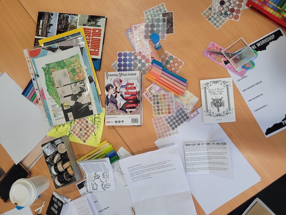 Bird's eye view of a table full of papers, stickers, coloured pens and some prompt worksheets for creating a zine.