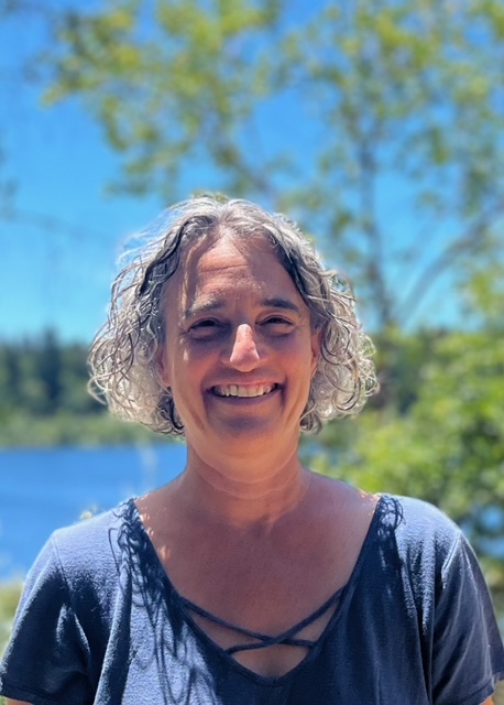 Jennifer Silverstein - LCSW has a chin-length bob haircut and is wearing a blue shirt standing outdoors in front of trees and water.