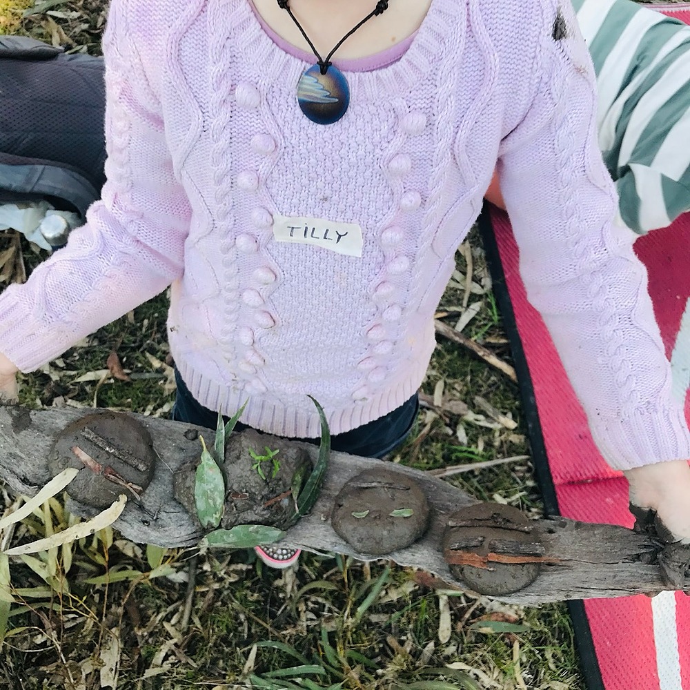 Child holding a bark with little mud faces on it